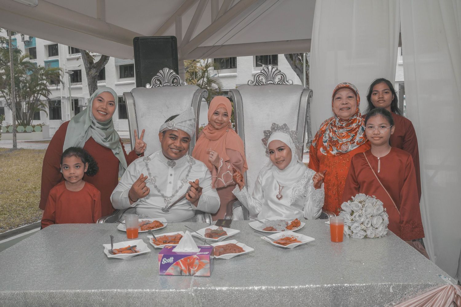 Family gathering at wedding reception with guests enjoying meal at outdoor table.