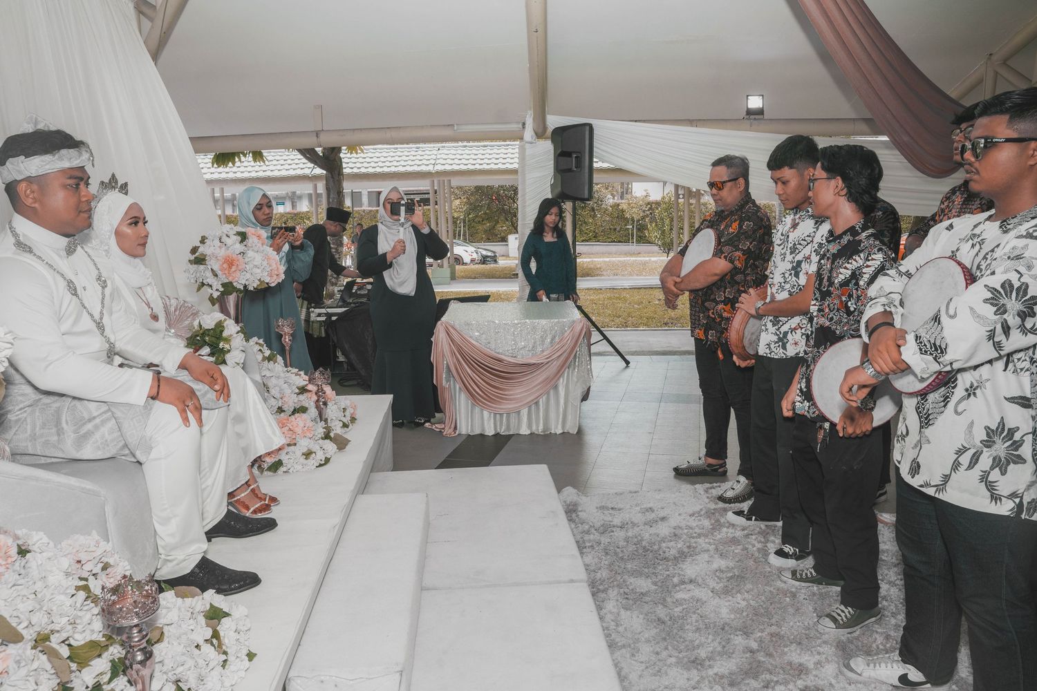 Wedding ceremony guests stand before newlyweds in decorated white tent venue with pink accents.