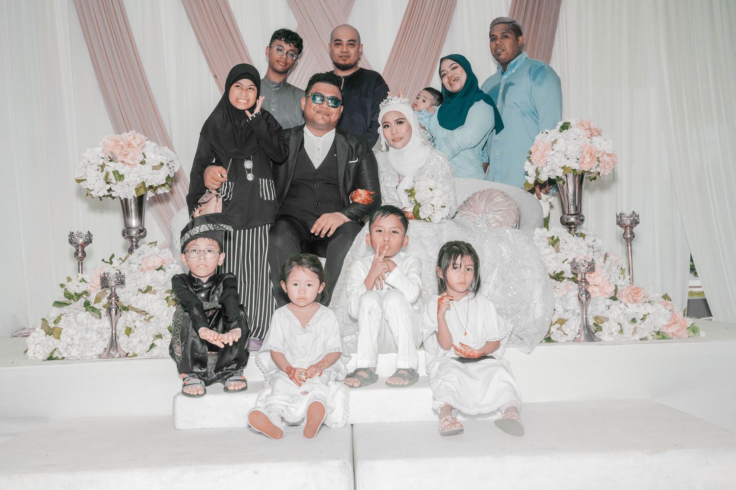 Family portrait of wedding guests in formal attire posed against floral backdrop.
