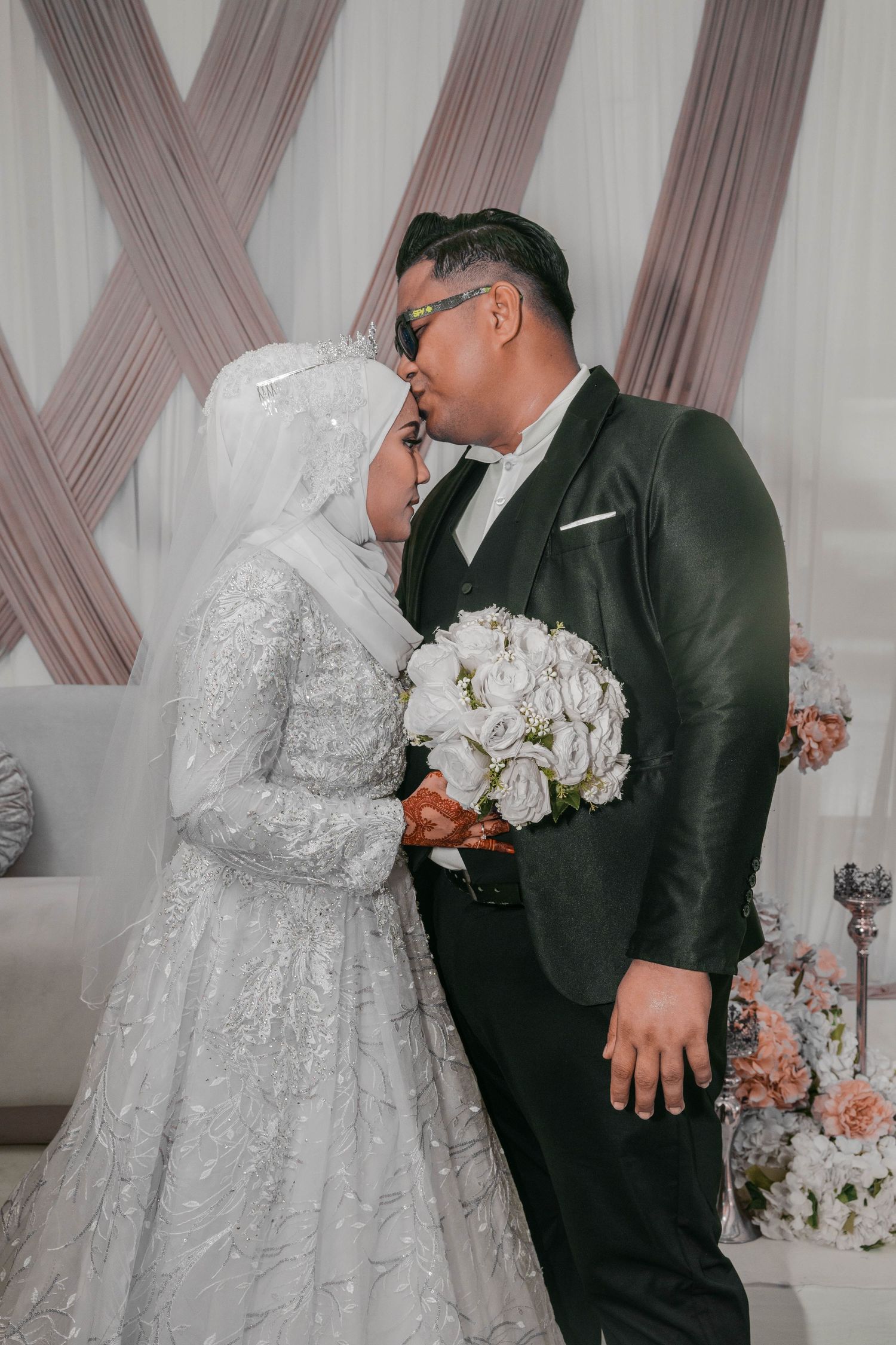 Intimate wedding moment captured against geometric backdrop with white floral arrangements.