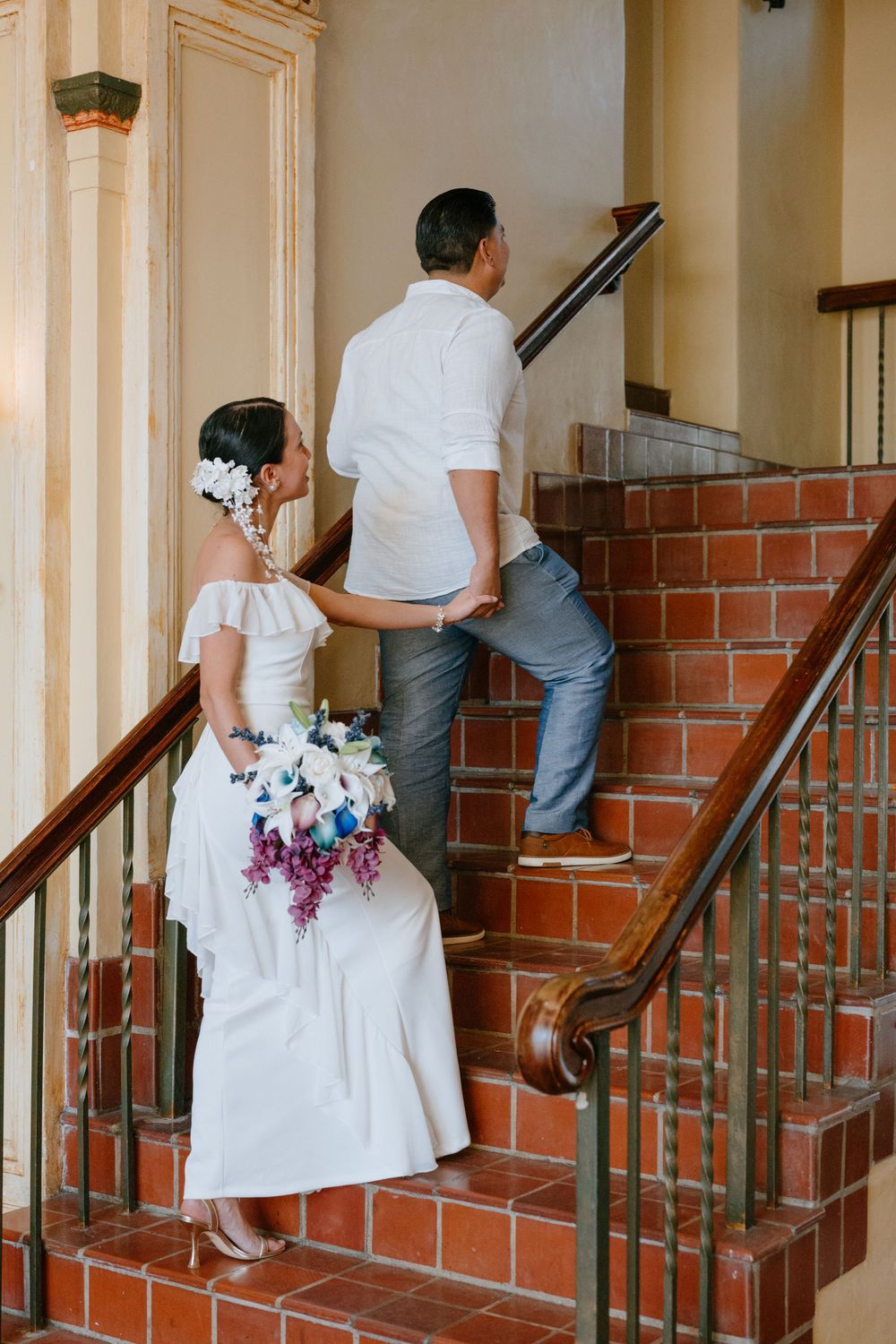 Couple ascending brick staircase with white wedding dress and colorful floral bouquet.