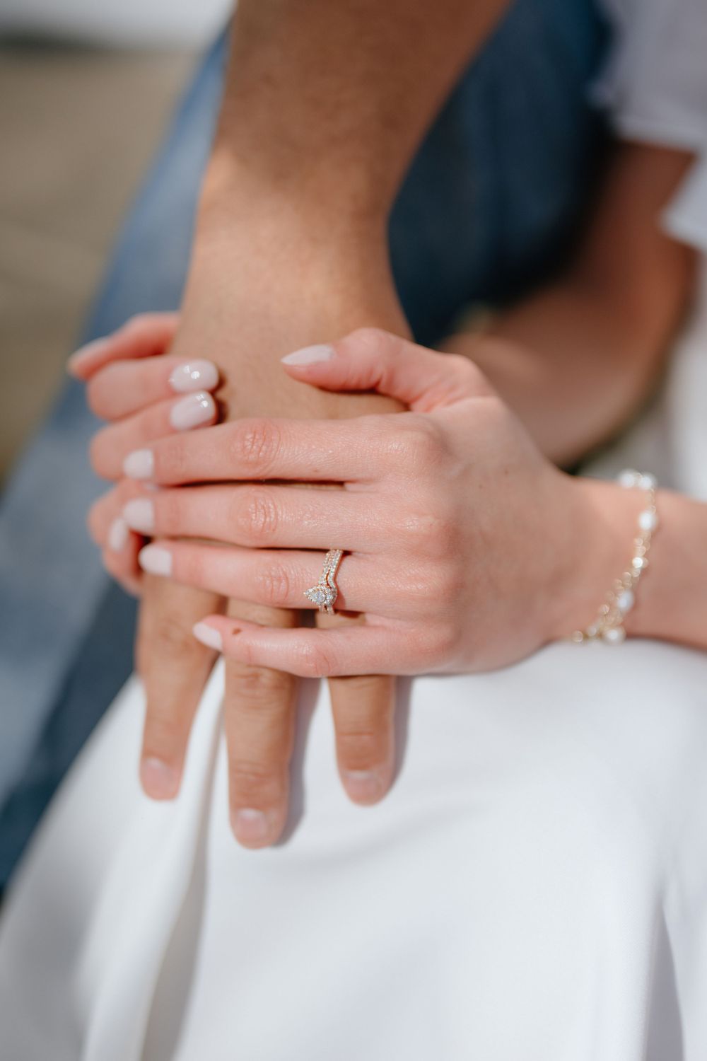 Close-up of wedding rings and clasped hands showing delicate jewelry details.