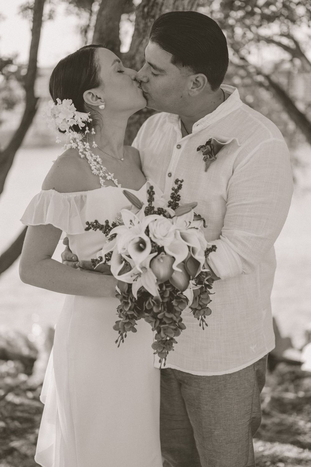 Black and white romantic wedding photo with floral bouquet and tropical backdrop.