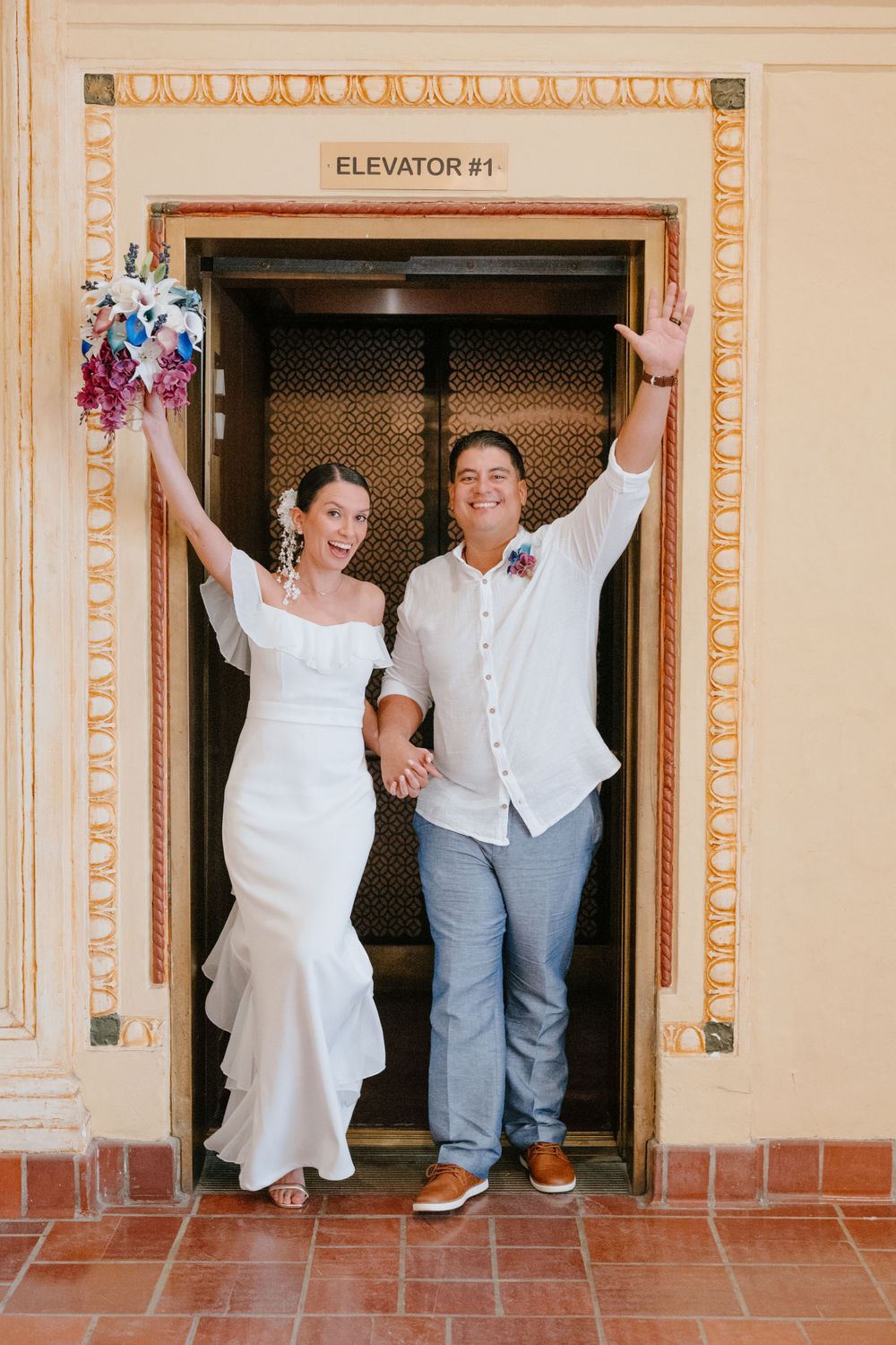 A joyful couple celebrates with raised arms in a beautifully framed elevator doorway.