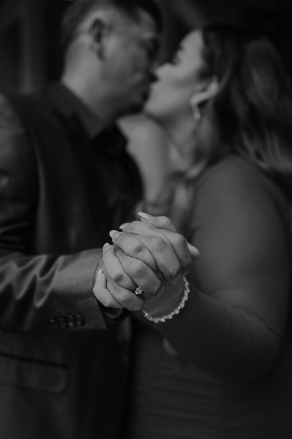 A black and white intimate portrait of a couple dancing, focusing on their clasped hands.