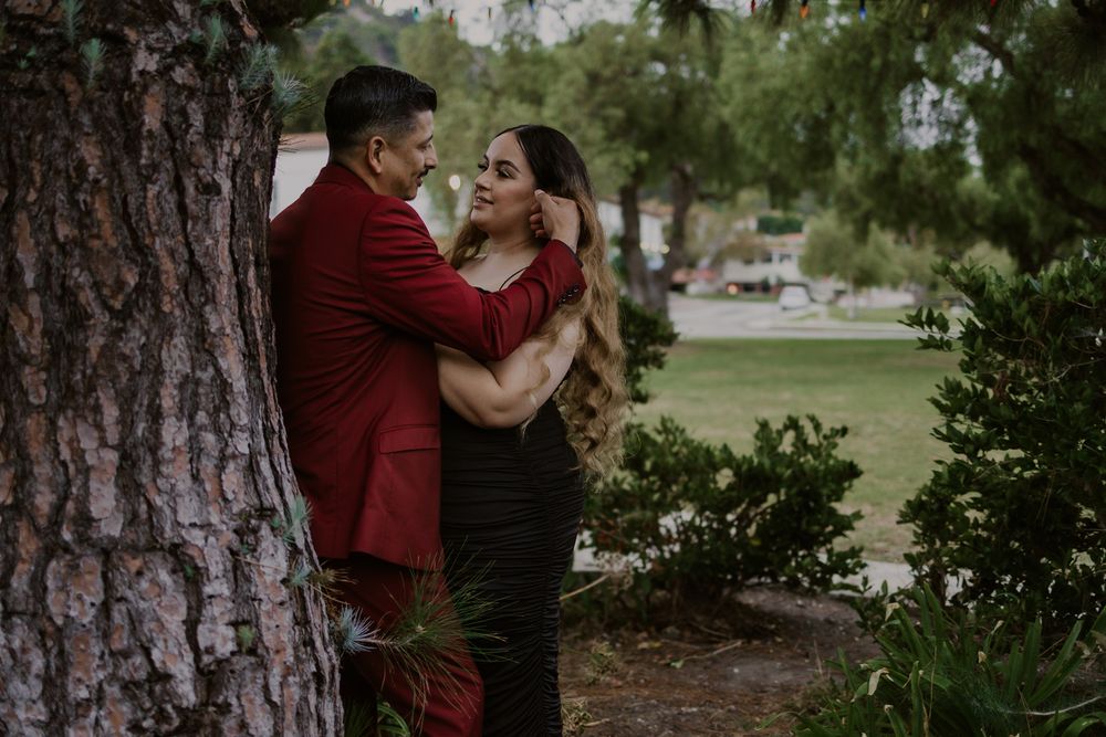 A couple shares an intimate embrace against a large tree trunk in a park setting.