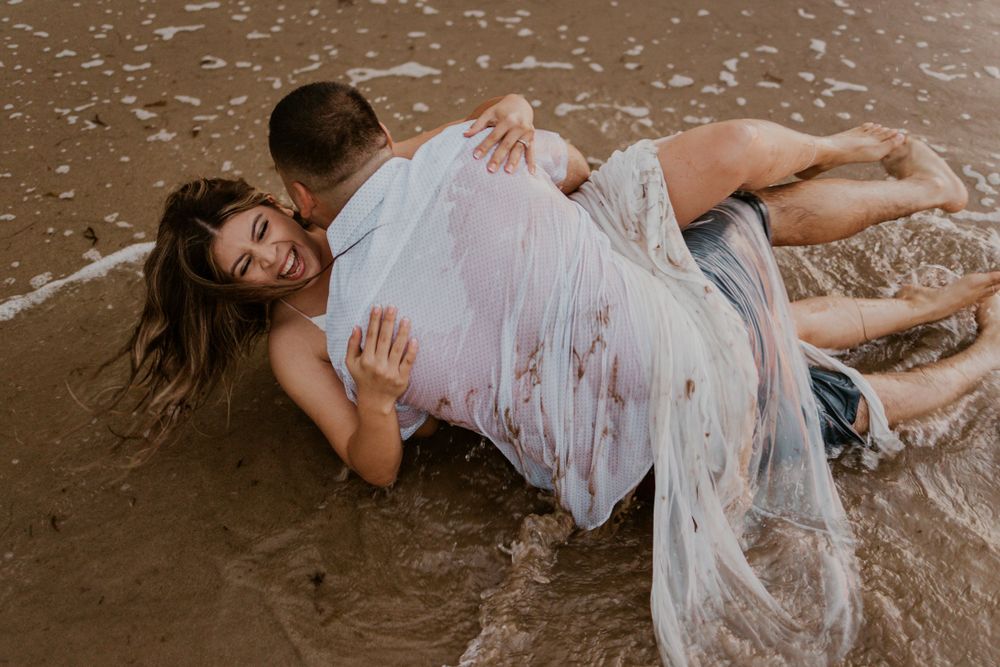 A couple lies in wet sand at the beach in romantic embrace.