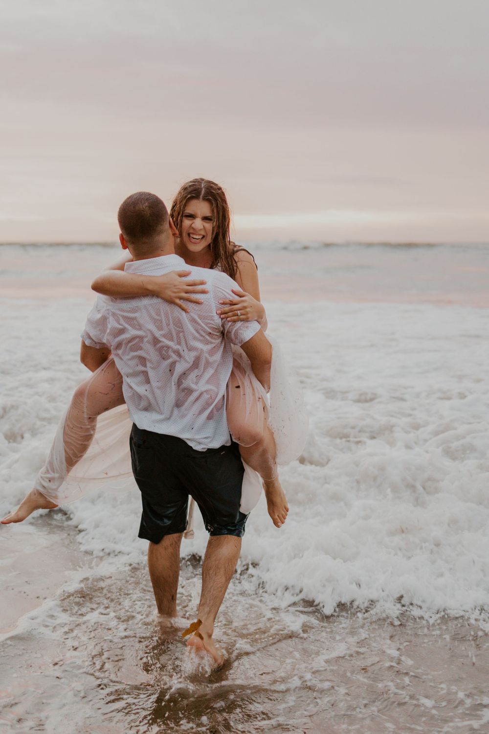 Playful couple splashing in ocean waves during sunset photoshoot.