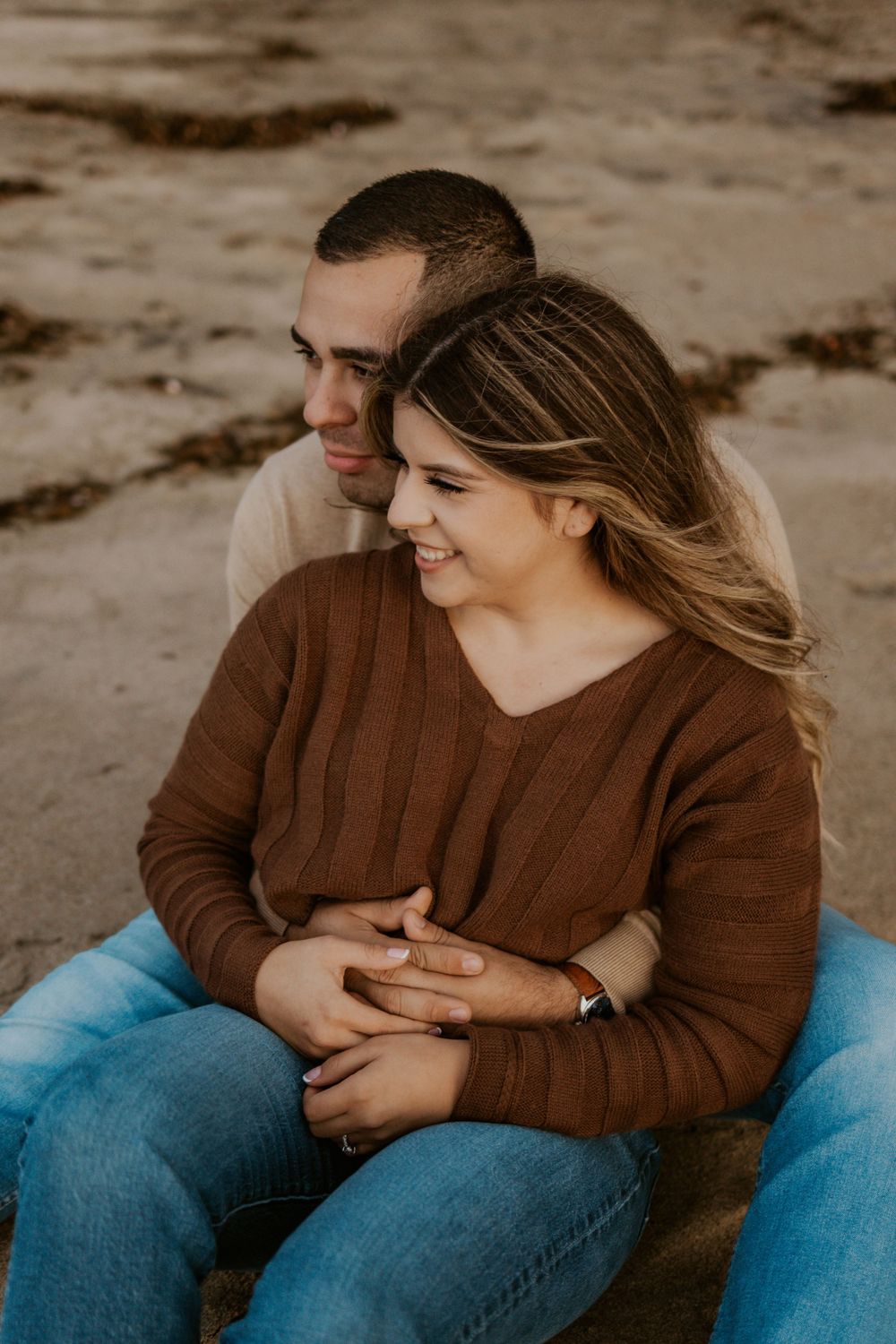 A cozy couple in brown sweaters embraces on the beach.