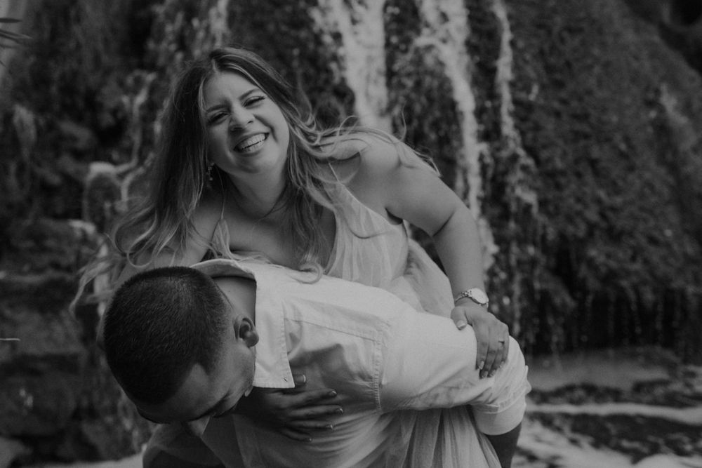 A playful black and white moment with a couple laughing near a waterfall.