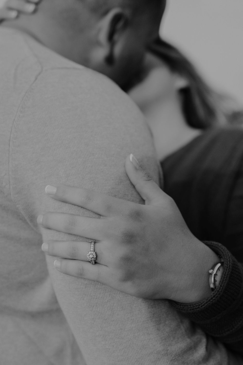 Close-up of an engagement ring as a couple embraces.