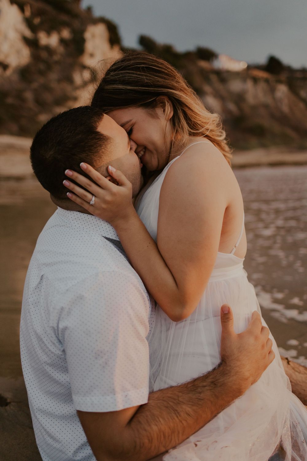 Intimate moment between couple in white outfits on beach at sunset.