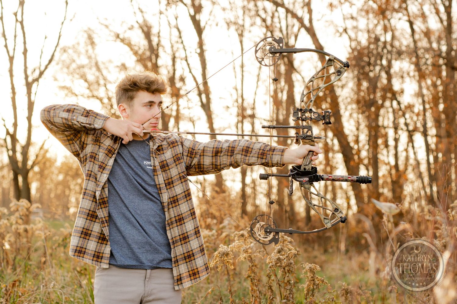 Archer in flannel shirt draws compound bow while practicing in autumn field.