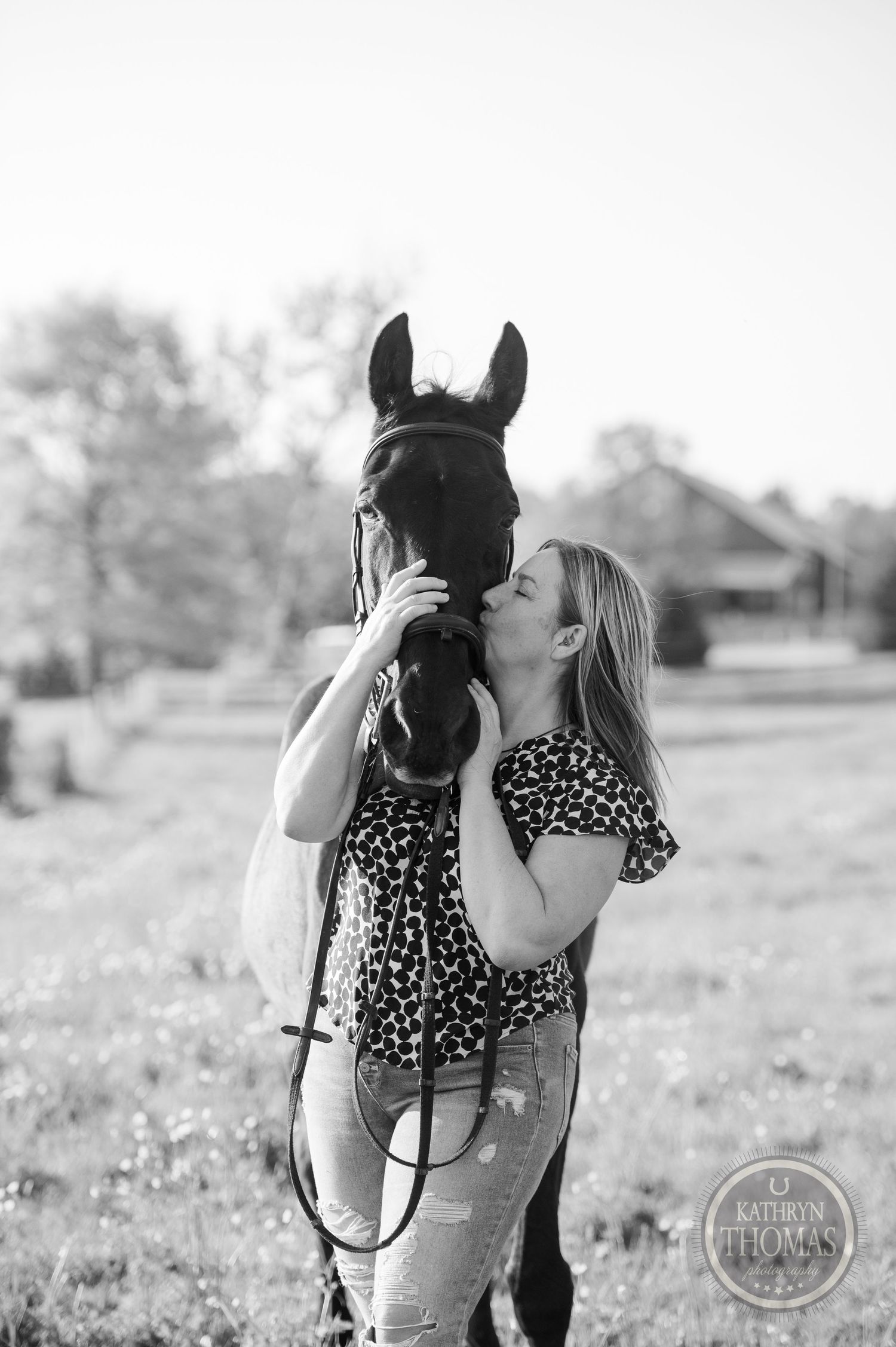 Black and white photo of woman embracing her horse's face tenderly in a pastoral setting.