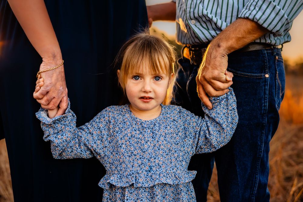 A small child in a floral dress holds hands with adults on either side.