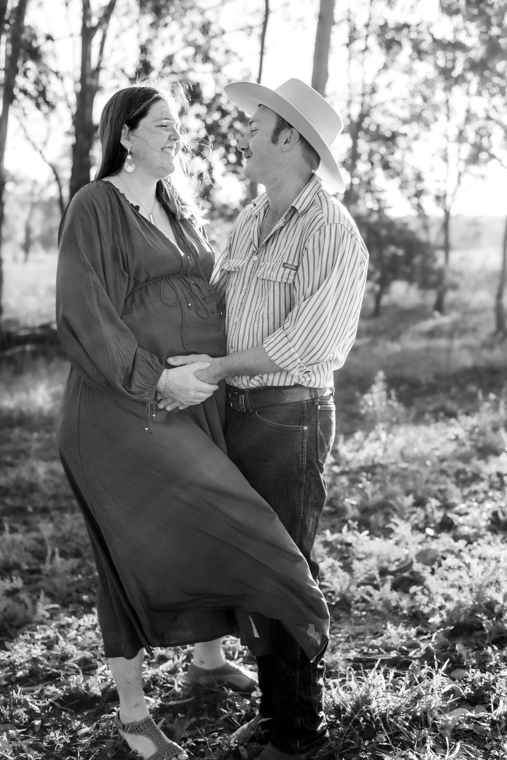 A black and white portrait of an expecting couple embracing in a wooded setting.