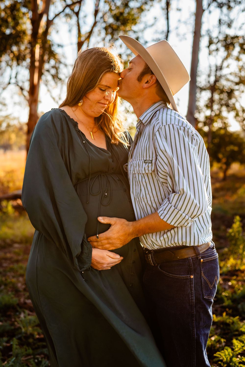 A romantic maternity photoshoot captures a couple's tender moment in golden sunlight.