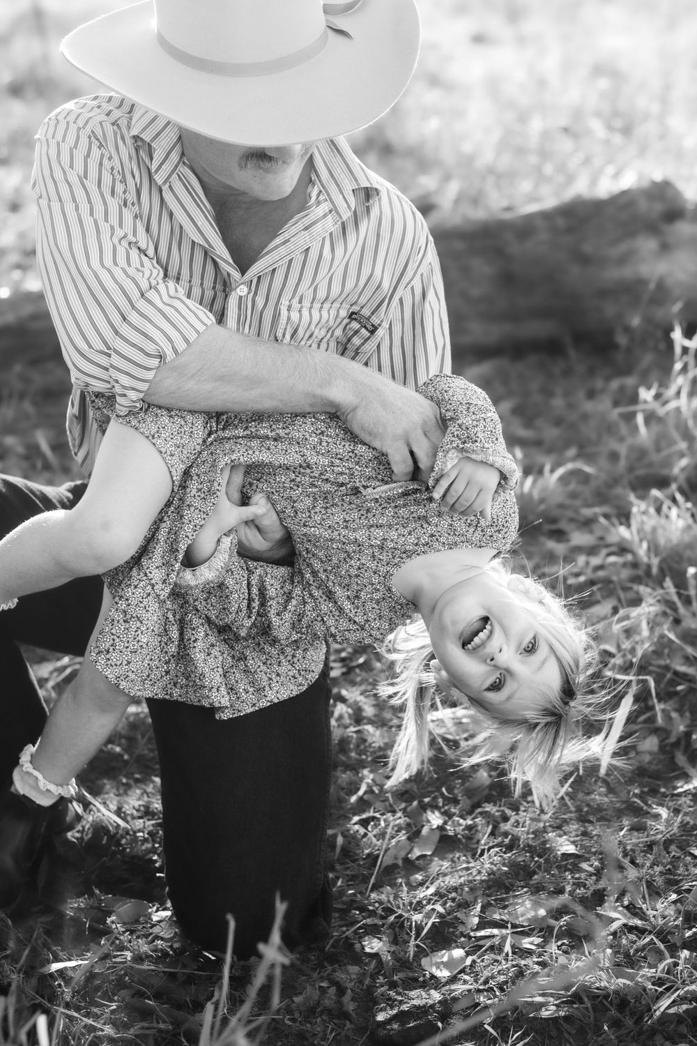A playful black and white portrait of a parent and child lying in autumn leaves.