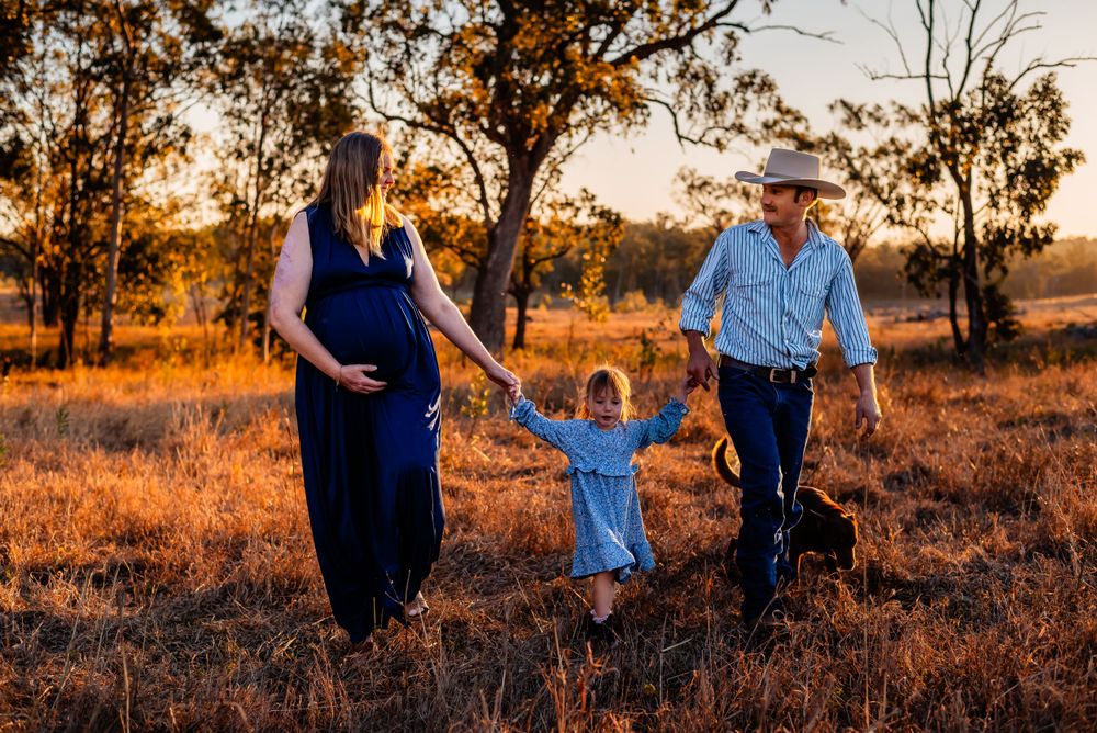 Family with young child walking hand in hand during sunset photoshoot in rural field.