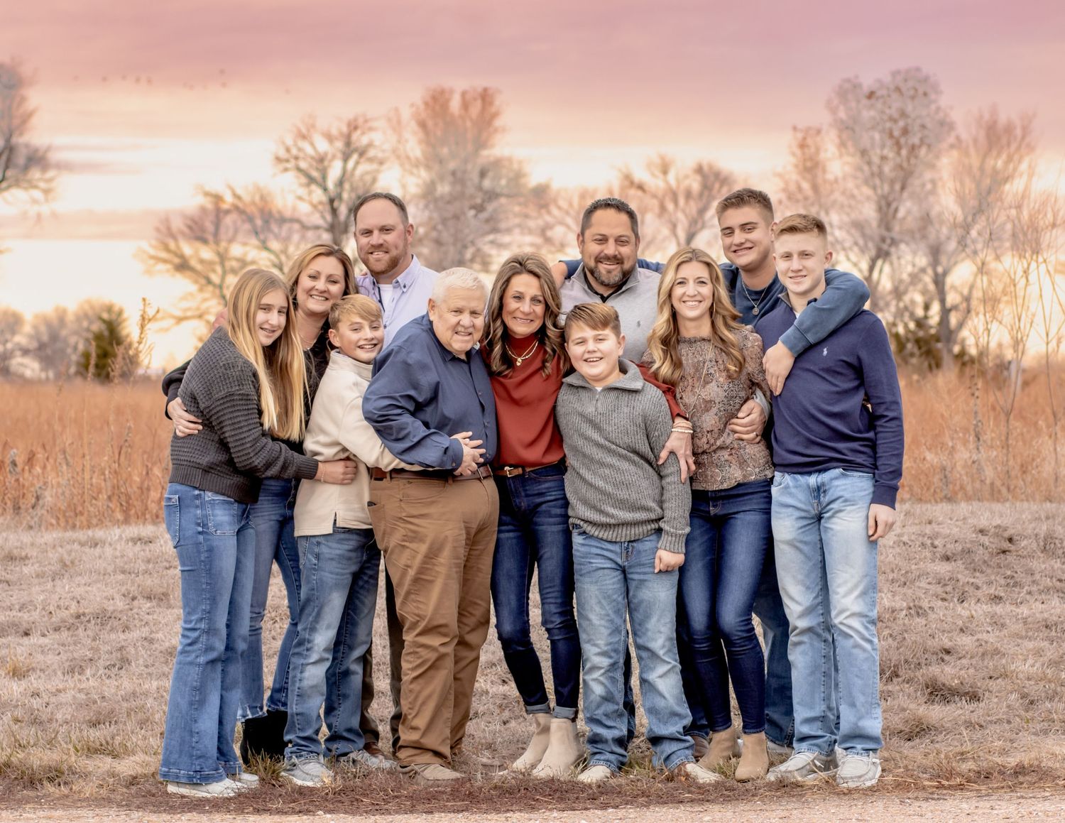 A group poses together outdoors against a backdrop of autumn trees during golden hour sunset.