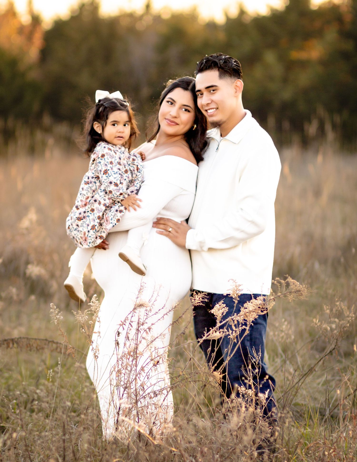 A family poses together in a golden field at sunset wearing coordinated white and floral outfits.