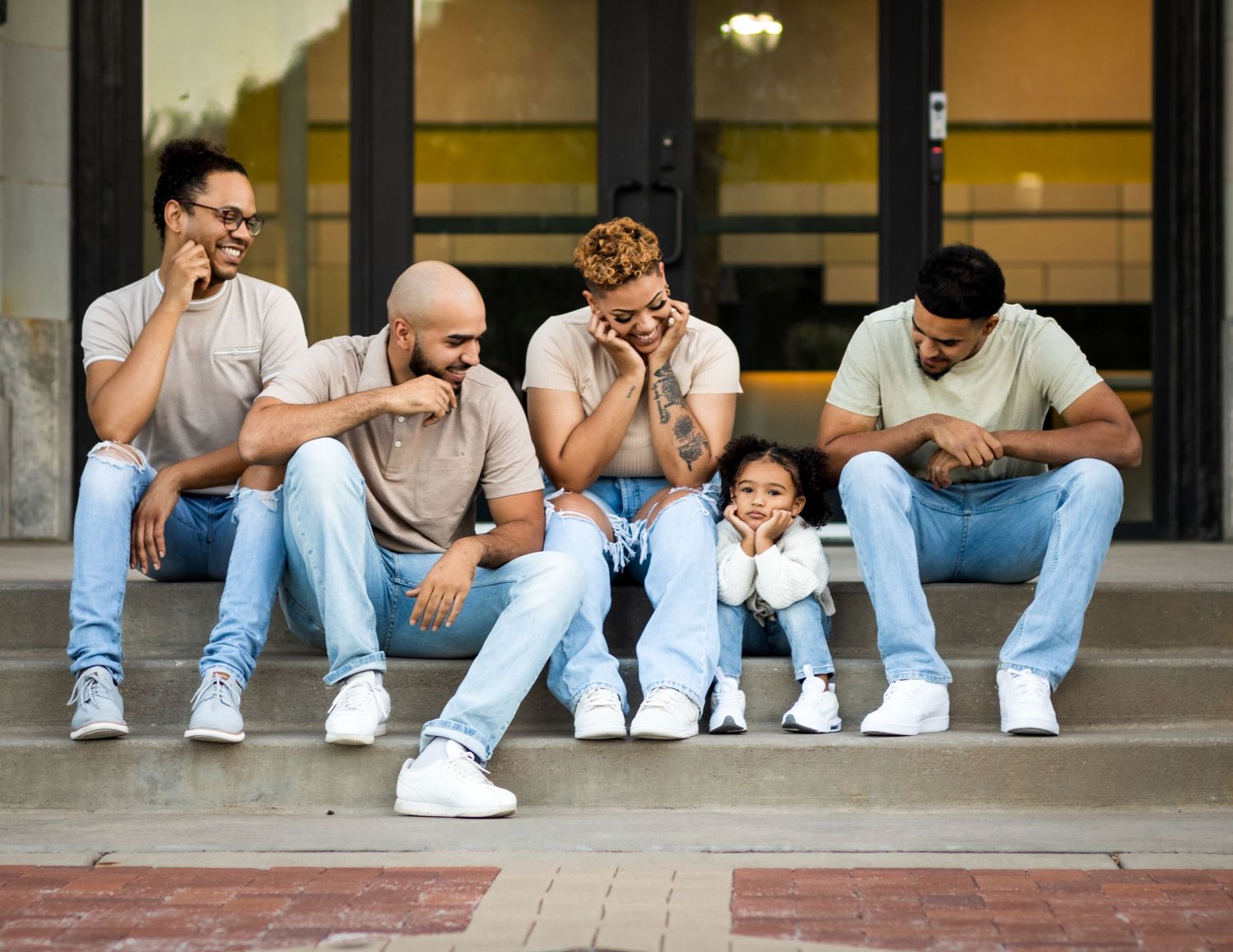 A group of friends sitting on steps wearing casual clothes and white sneakers, holding their heads in yawning poses.