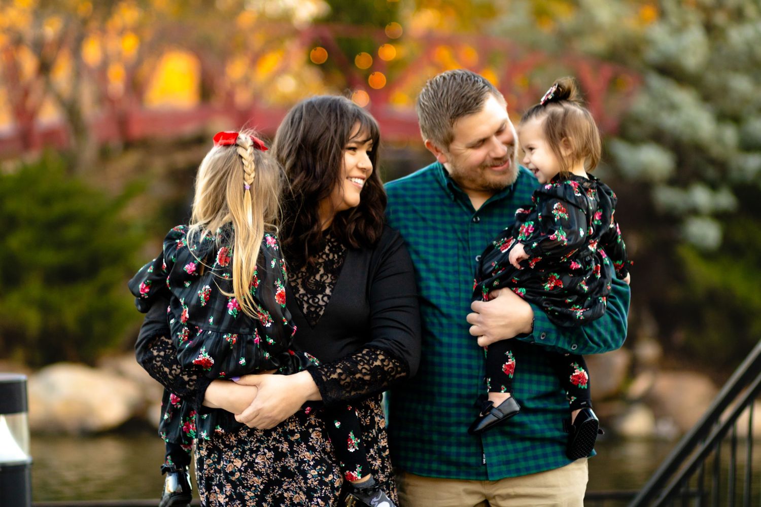 Family wearing floral and teal outfits poses together outside during golden hour near autumn foliage.