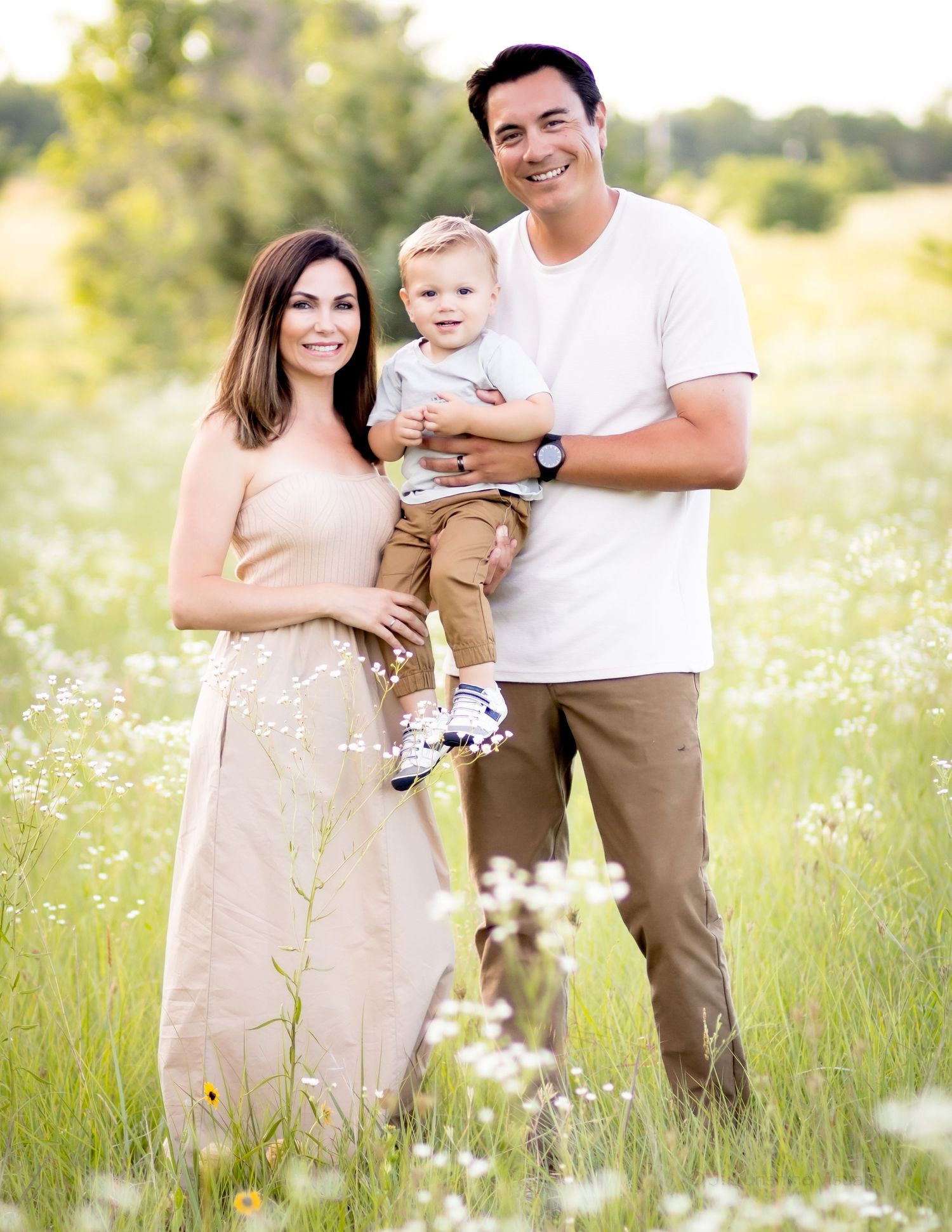A family poses together in a sunlit meadow with wildflowers on a warm summer day.