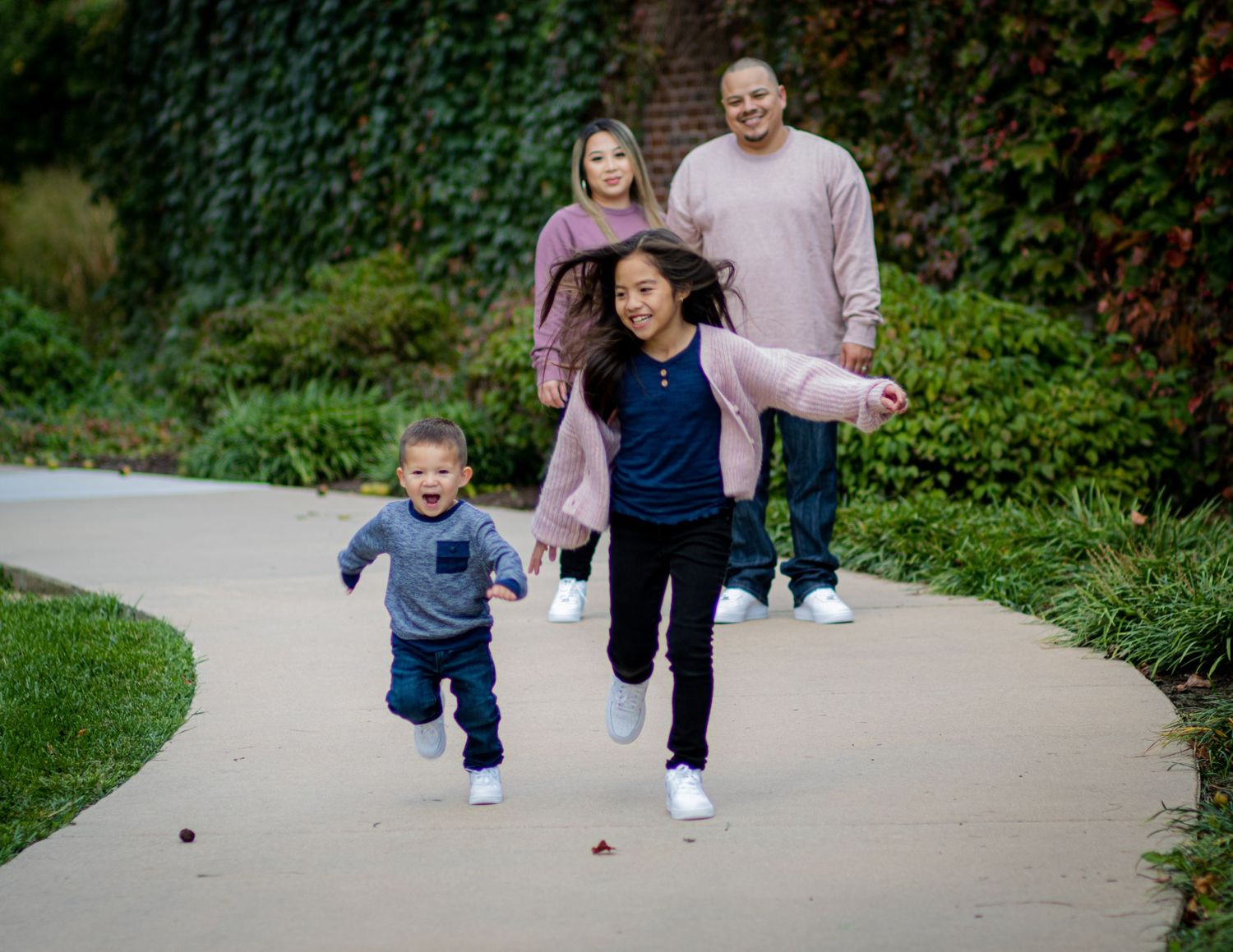 Family enjoying a playful moment running together on a curved garden path surrounded by lush green foliage.