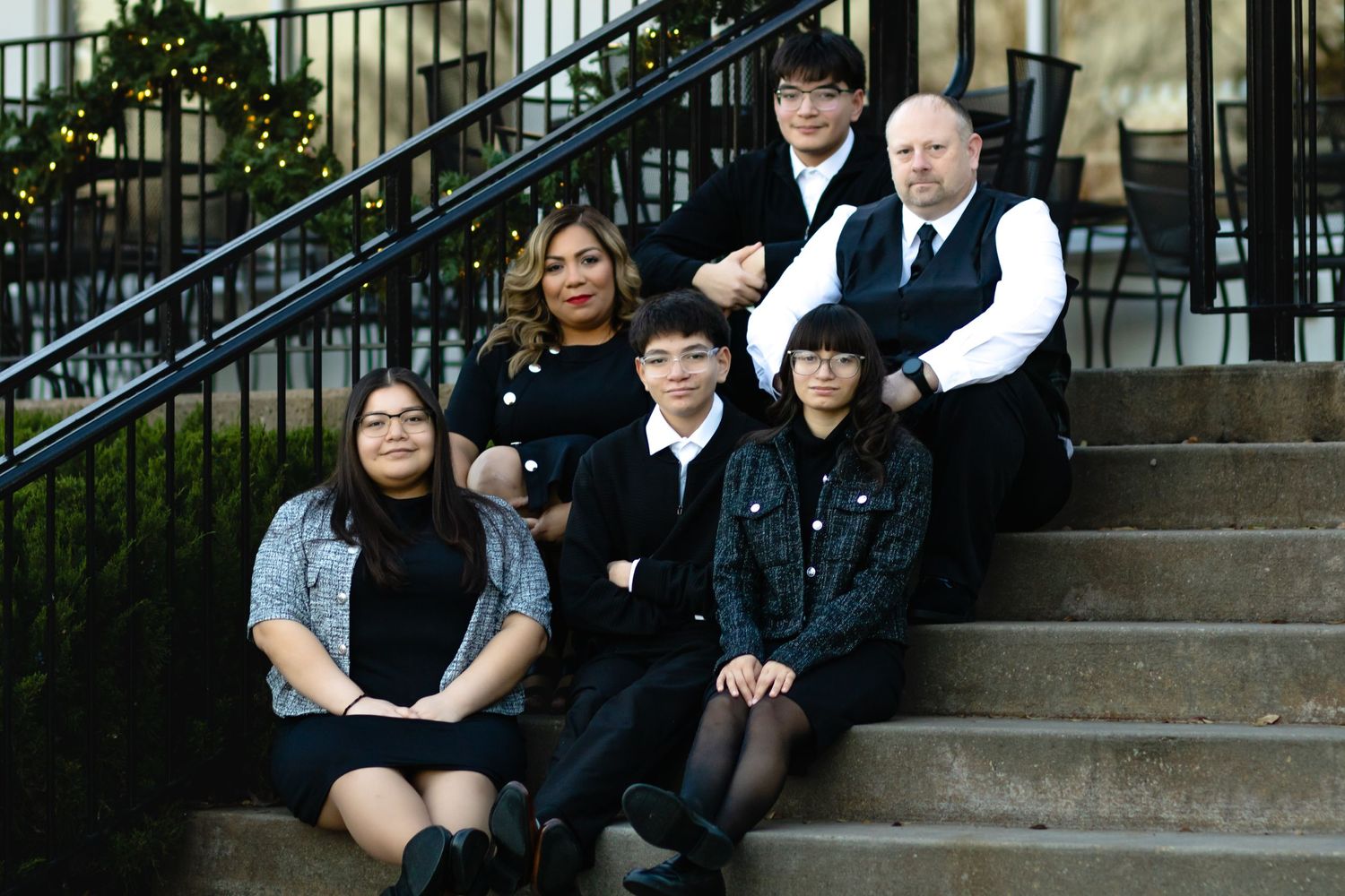 A group in black and white attire poses together on stone steps outside a building with wrought iron railings.