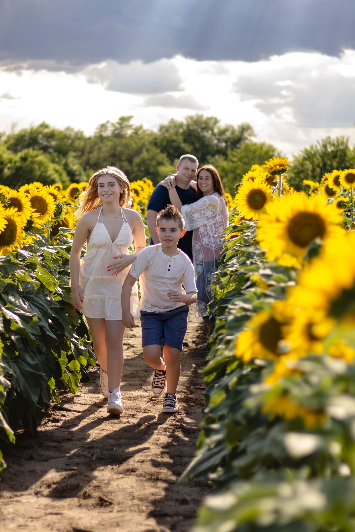 People walking together through a vibrant sunflower field under dramatic cloudy skies on a summer day.