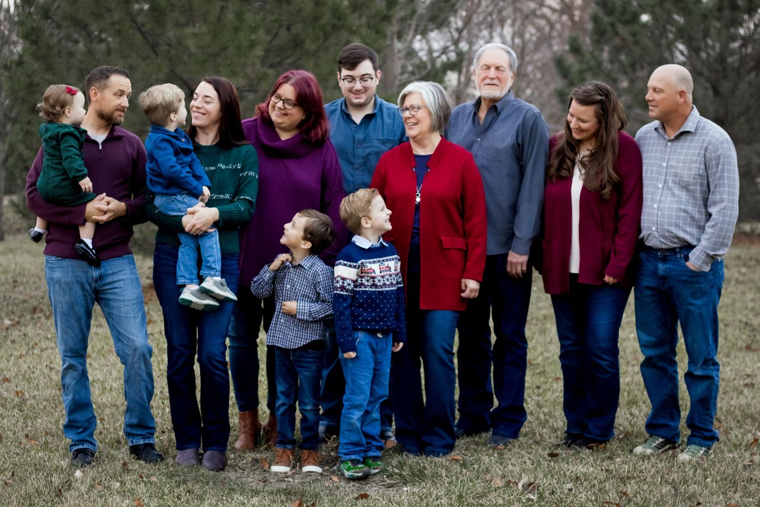 Multi-generational family group wearing coordinated blue and red outfits poses together outdoors against blurred natural background.