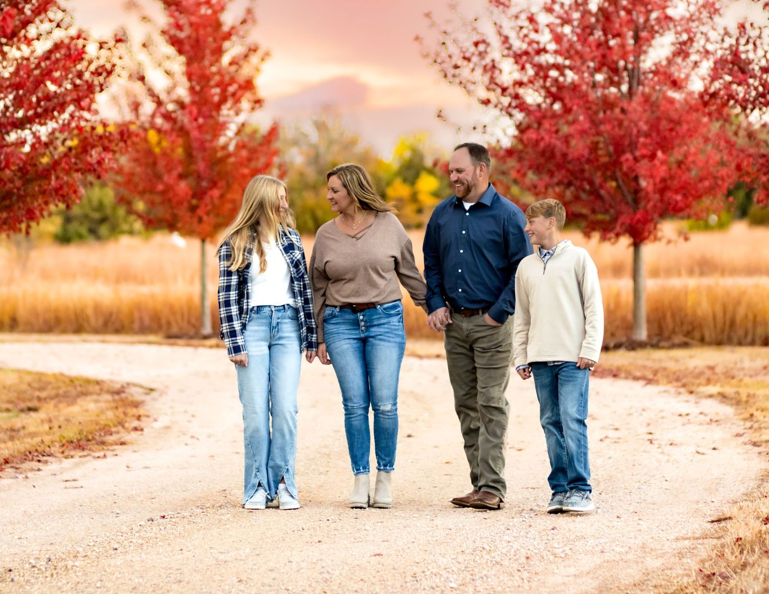 A group walks together on a dirt path surrounded by vibrant red autumn trees at sunset.