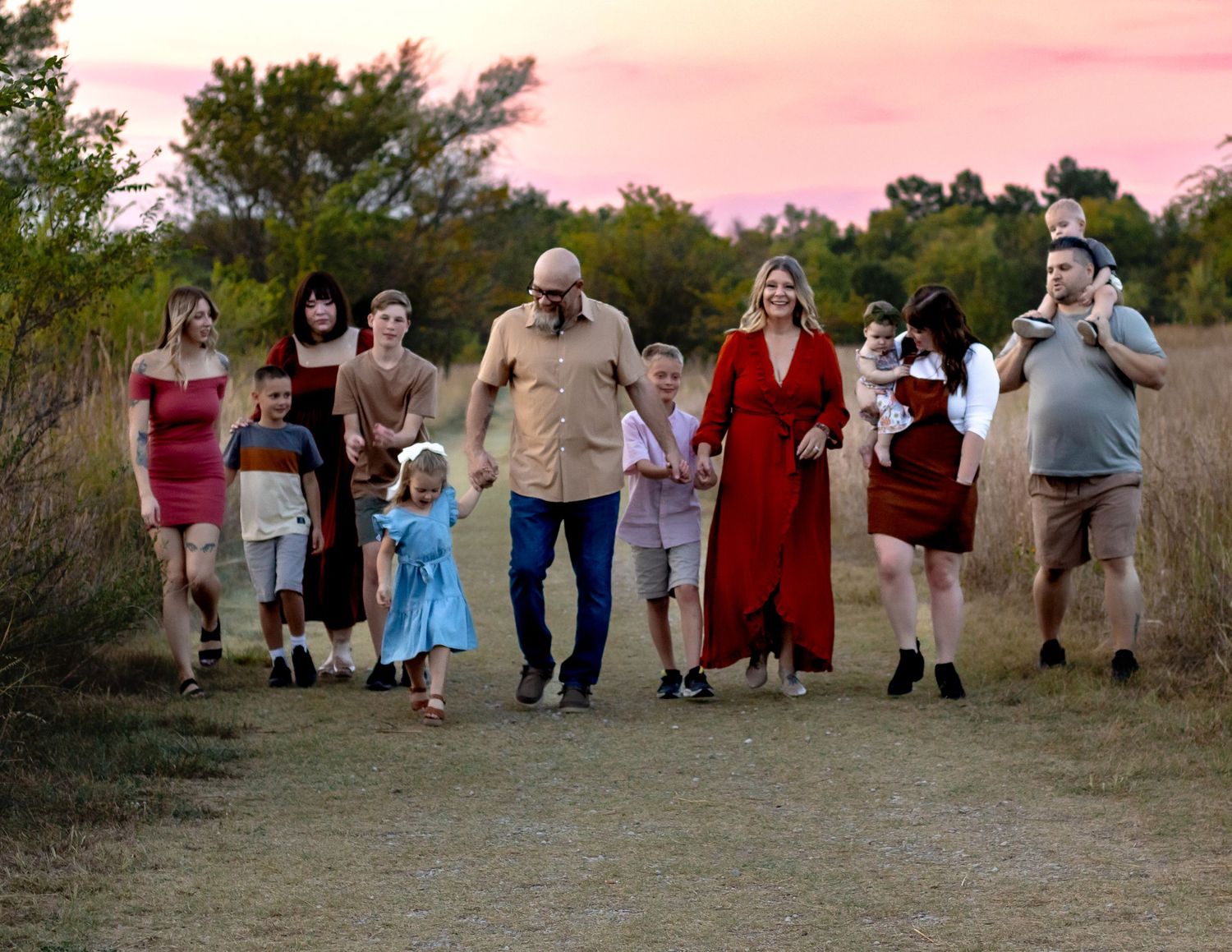 A group of people walking together on a dirt path at sunset with trees in the background.