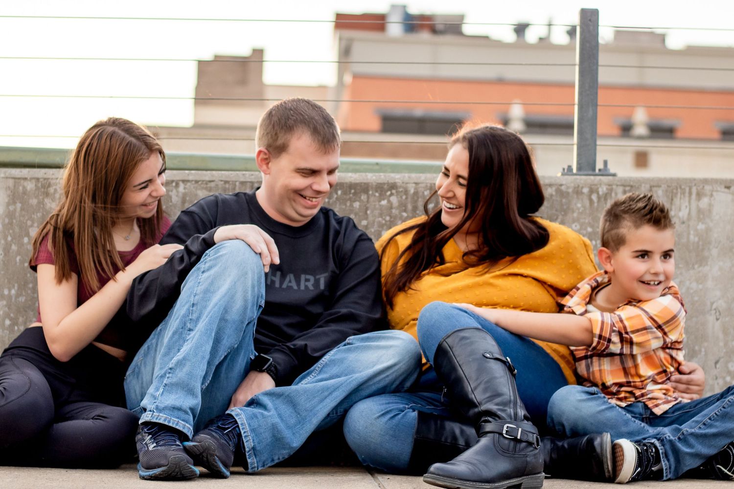 Four people sitting casually together on a concrete surface laughing and enjoying each other's company.