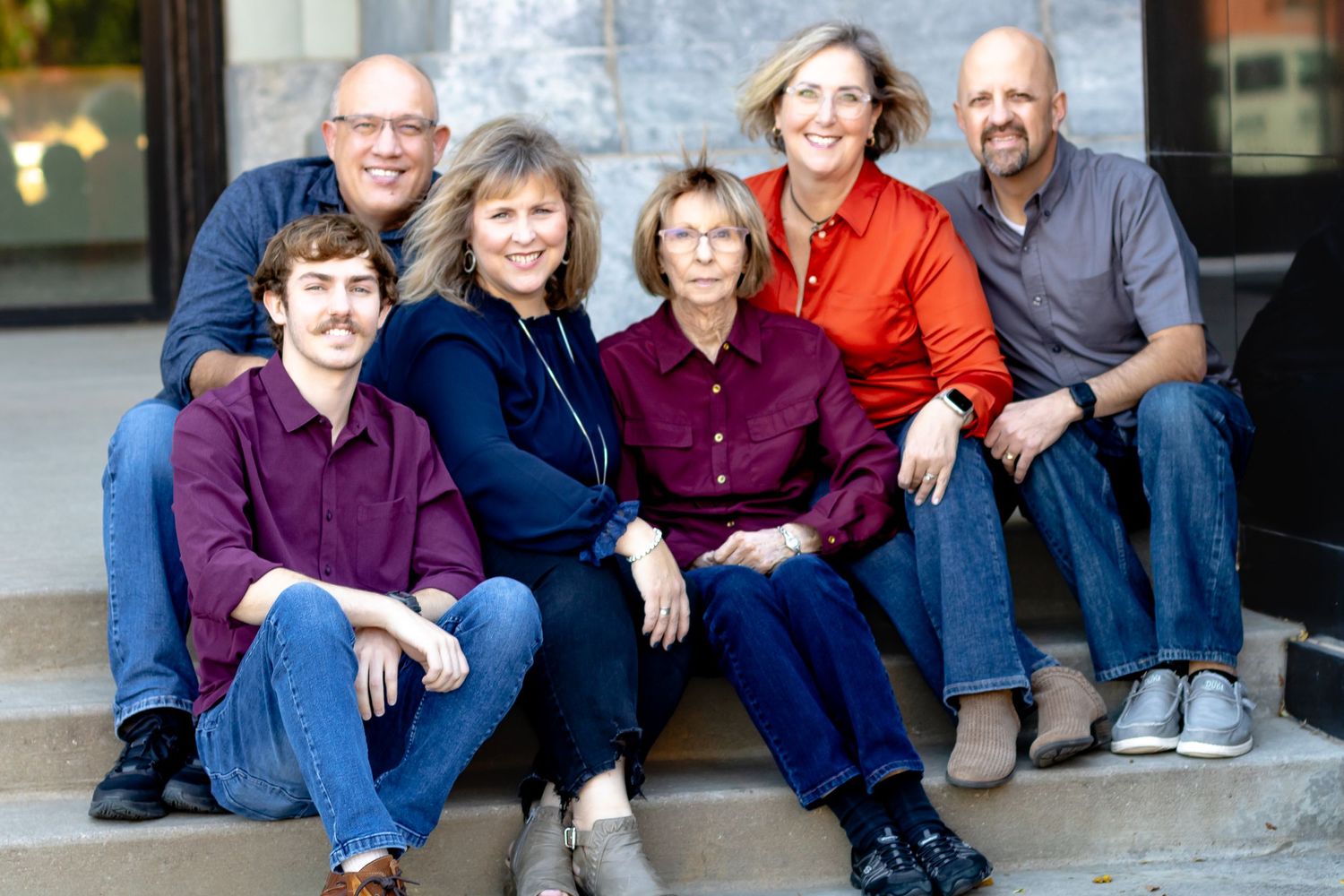 A group of people sitting together on stone steps wearing casual clothing in different shades of blue and purple.