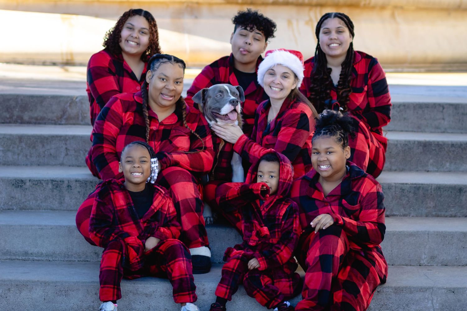 Group wearing matching red and black buffalo plaid holiday pajamas sitting together on outdoor steps.