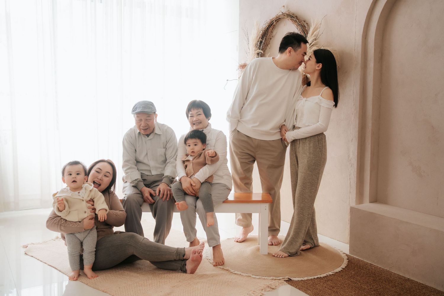 A family in neutral-colored clothing sits together on a beige carpet in a minimalist white room一家人穿著中性色系服裝，坐在極簡主義白色房間的米色地毯上。