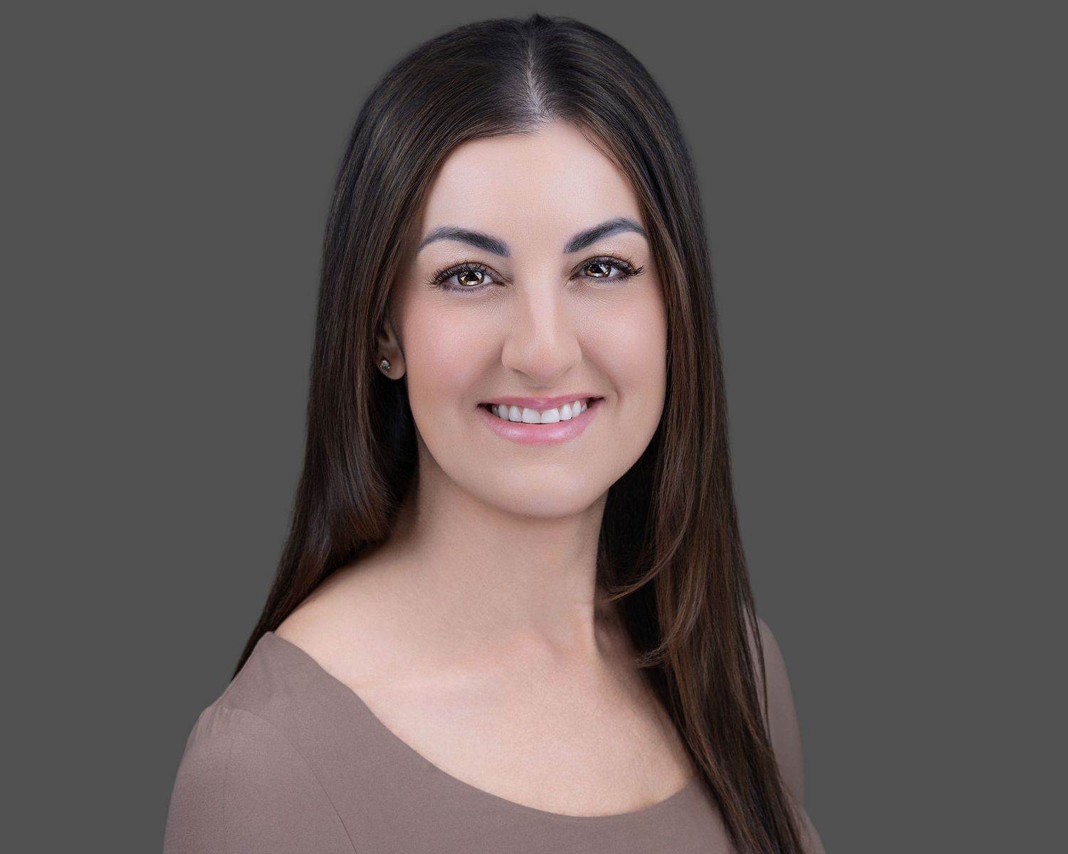 Professional headshot of woman with long dark hair against gray background.