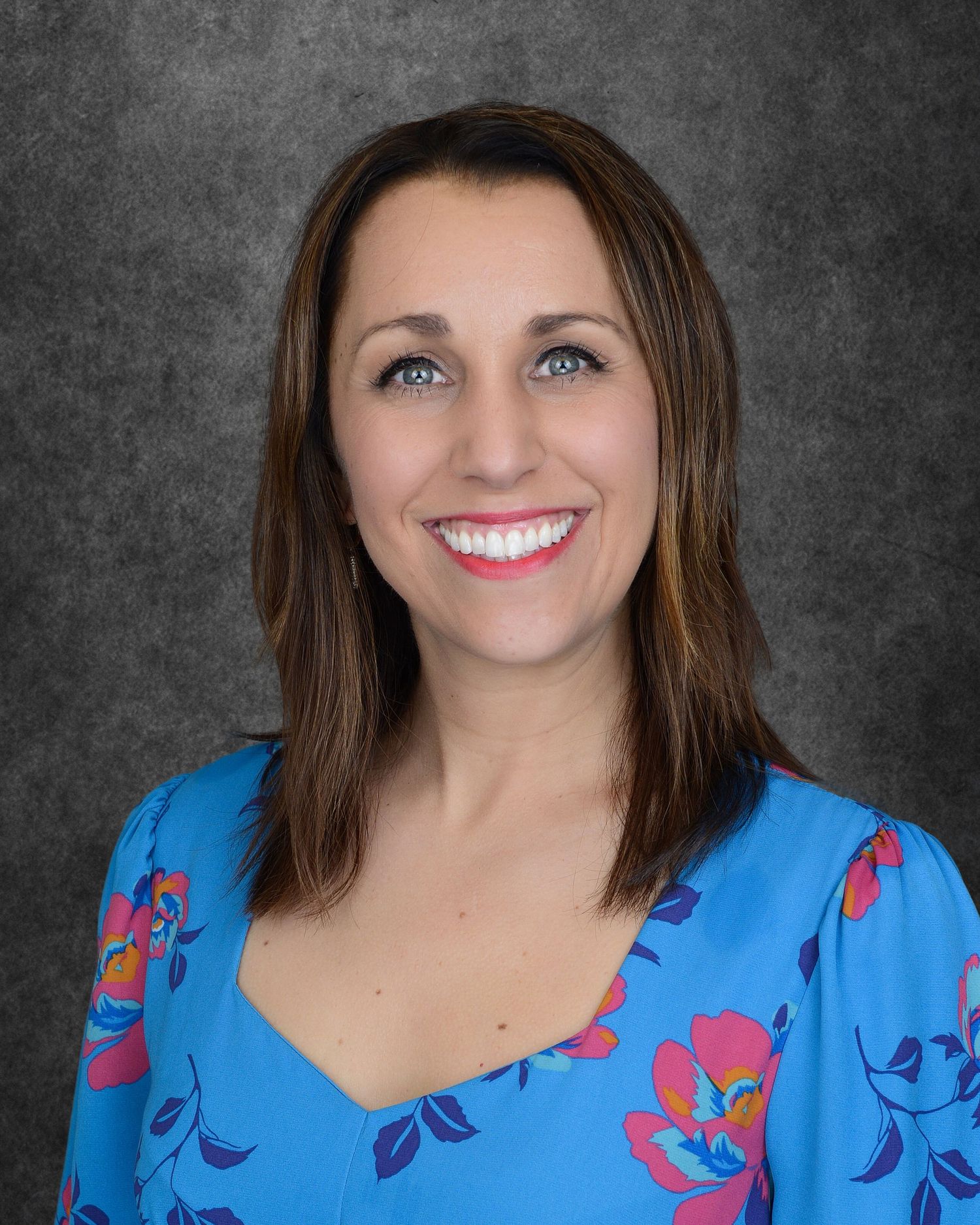 Professional headshot of person in blue floral top against dark gray background.