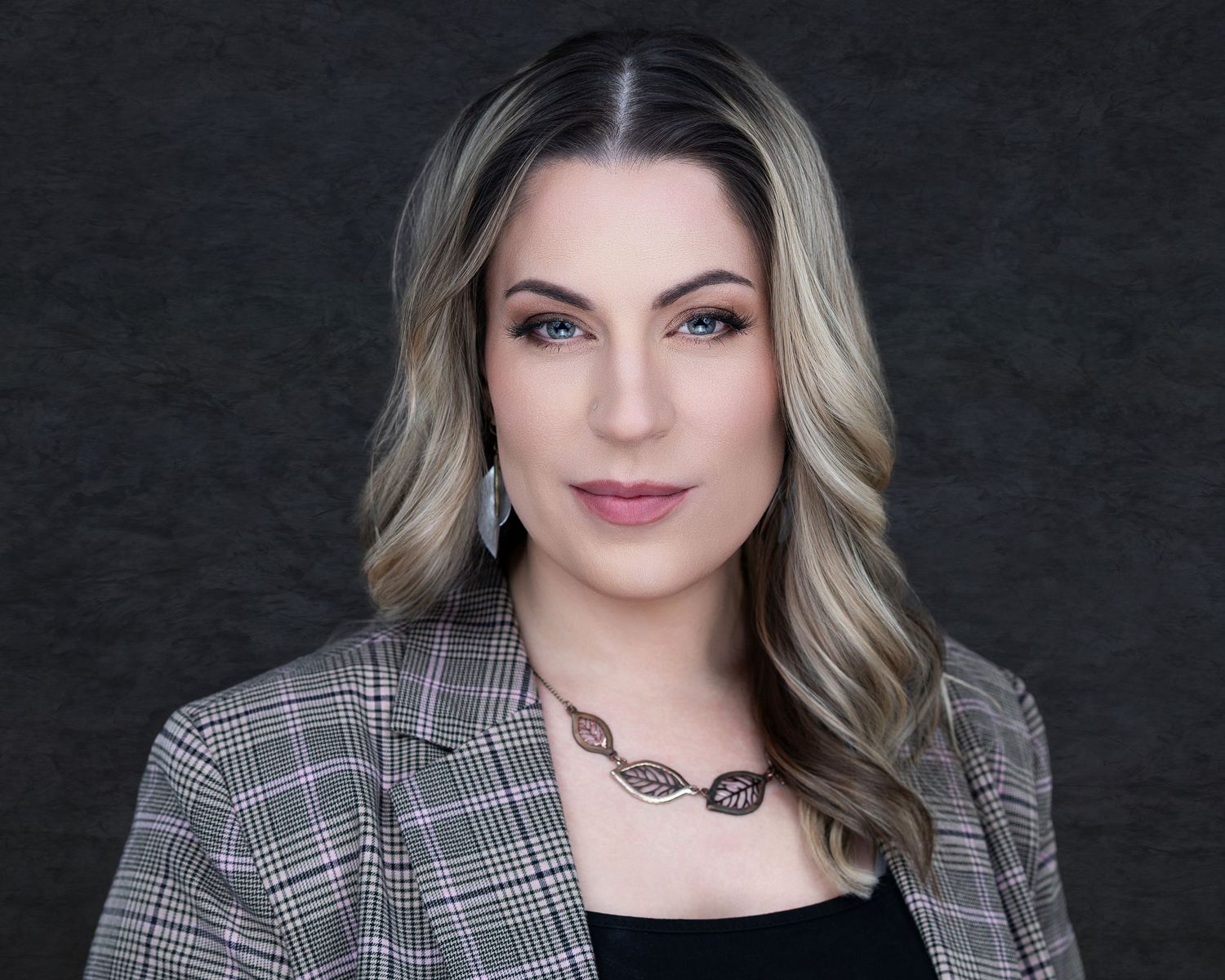Corporate headshot featuring plaid blazer and dark top against neutral background.