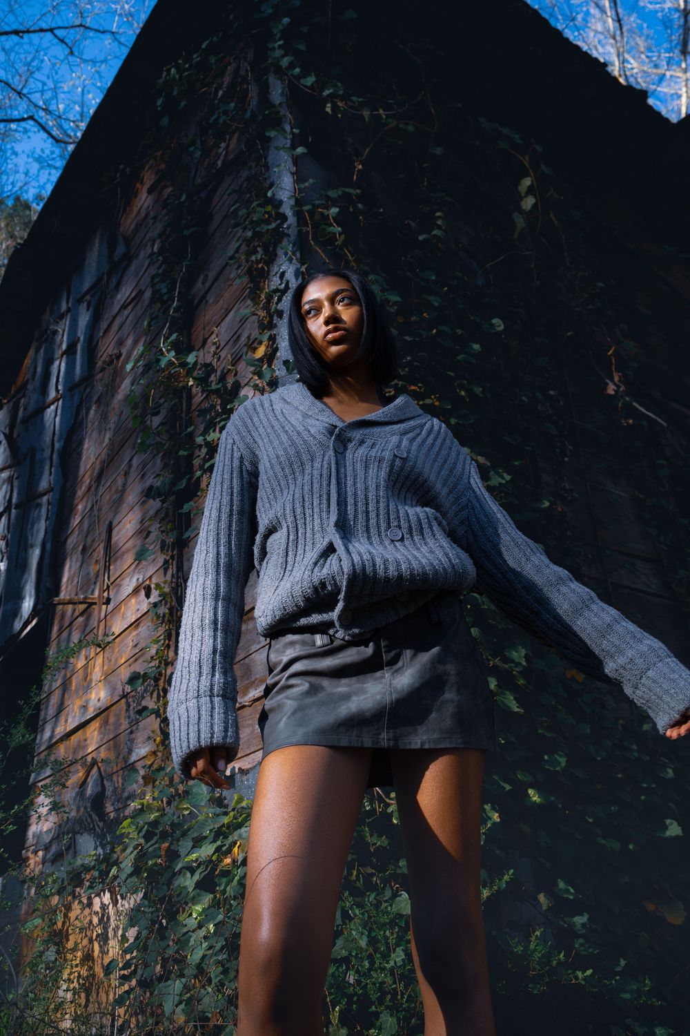 A person in a gray sweater poses against a dark building wall with climbing vines in a multi-frame photo series.