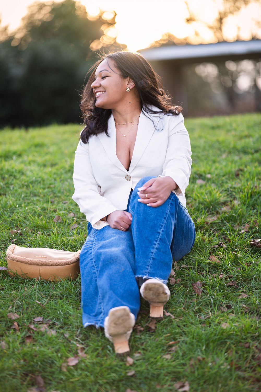 Person in white shirt and blue jeans relaxes on grassy hill during golden sunset.