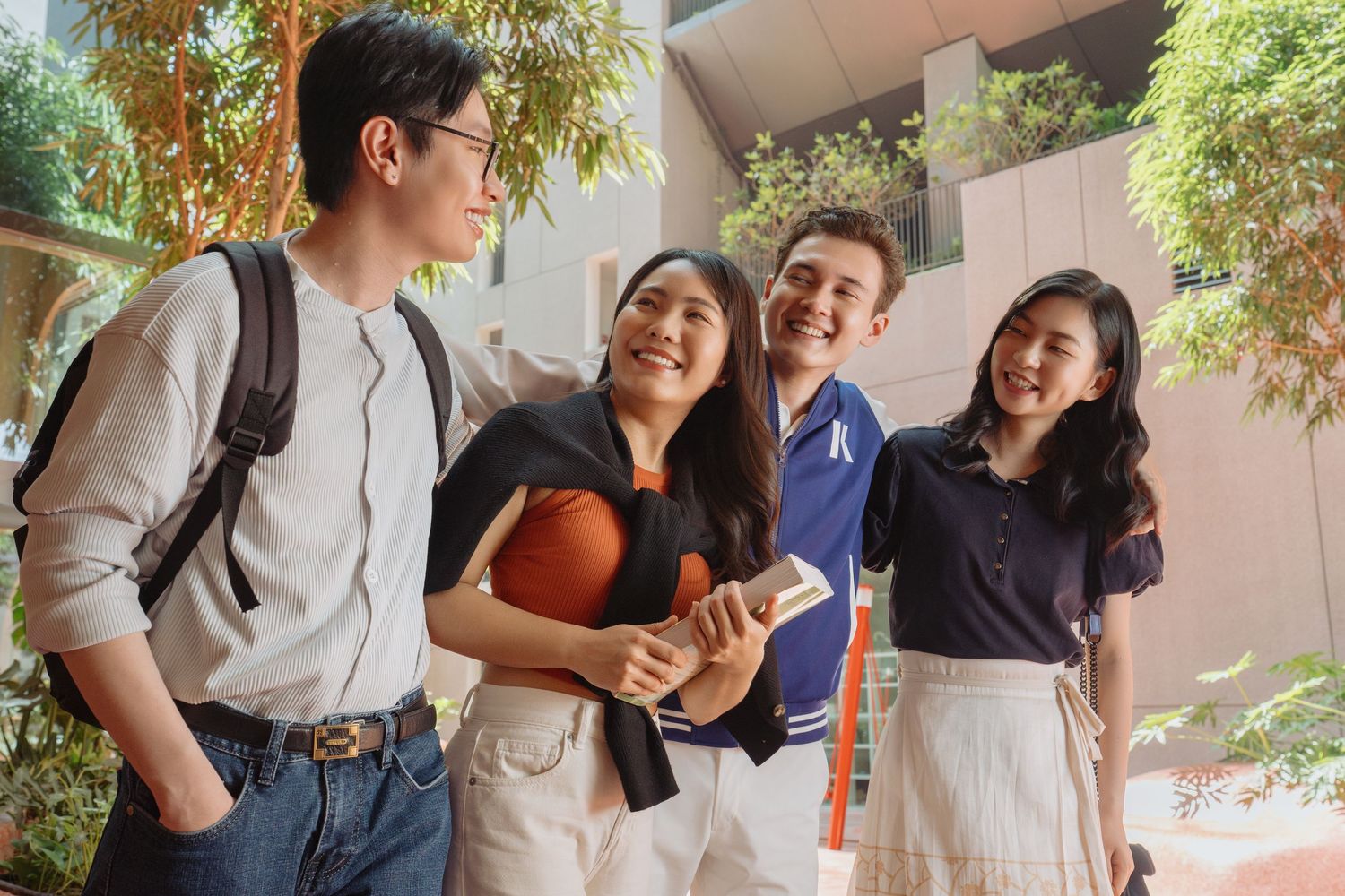 A group of young students laughing together on campus while holding books and backpacks.