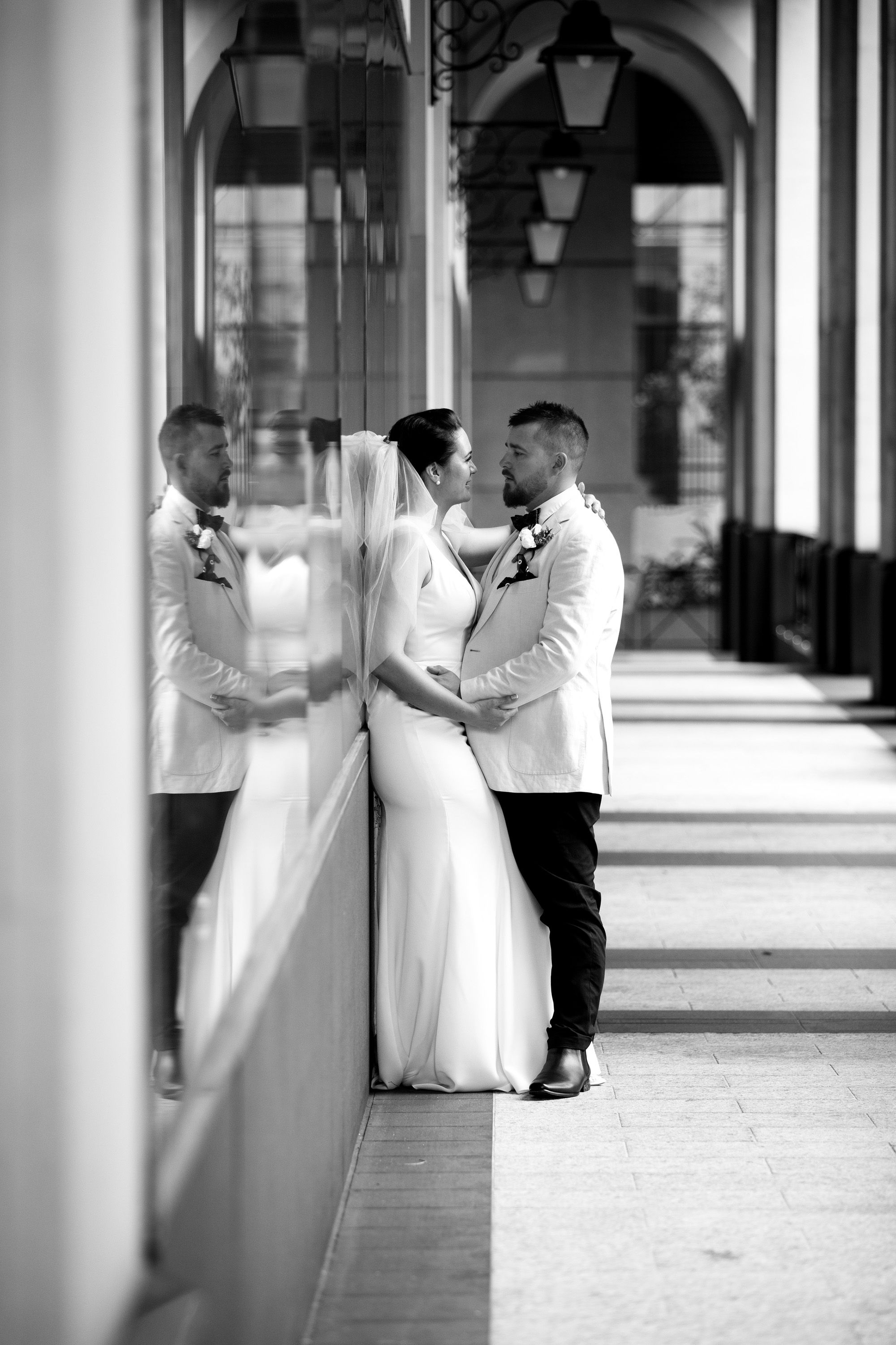 Black and white photo of bride and groom kissing beside a reflective column in an archway.