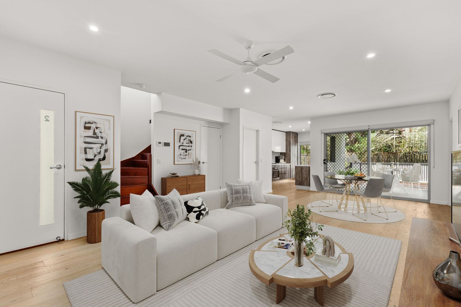 Modern white living room with timber floors, ceiling fan, white sofa, and glass doors leading to an outdoor entertaining area.