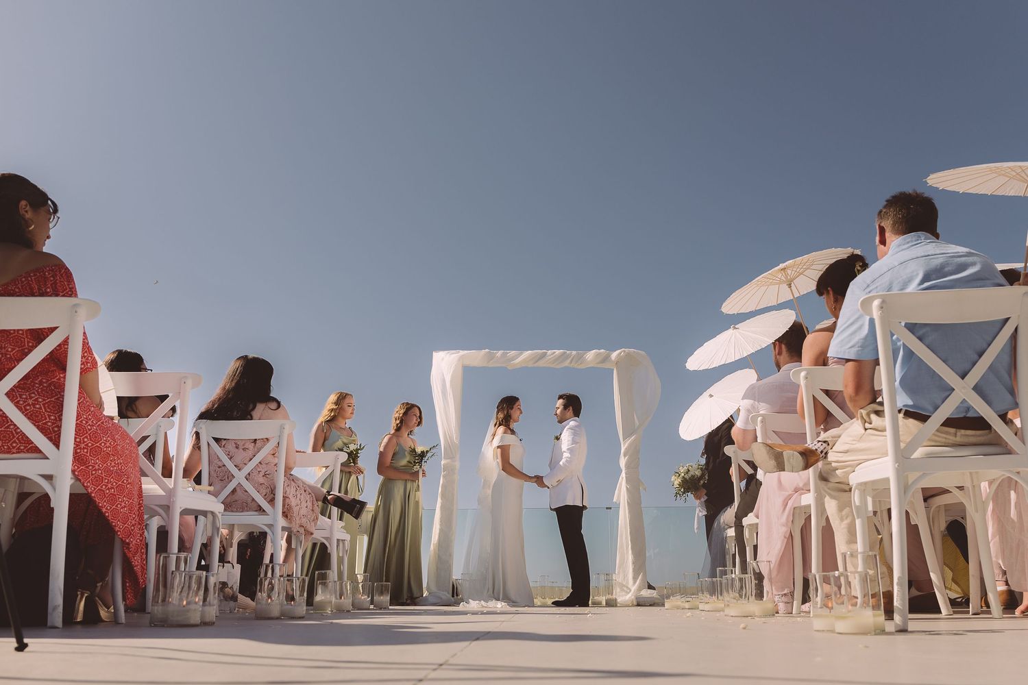 Low angle view of an outdoor destination wedding in Santorini as the couple face each other that the alter and sky as a backdrop.