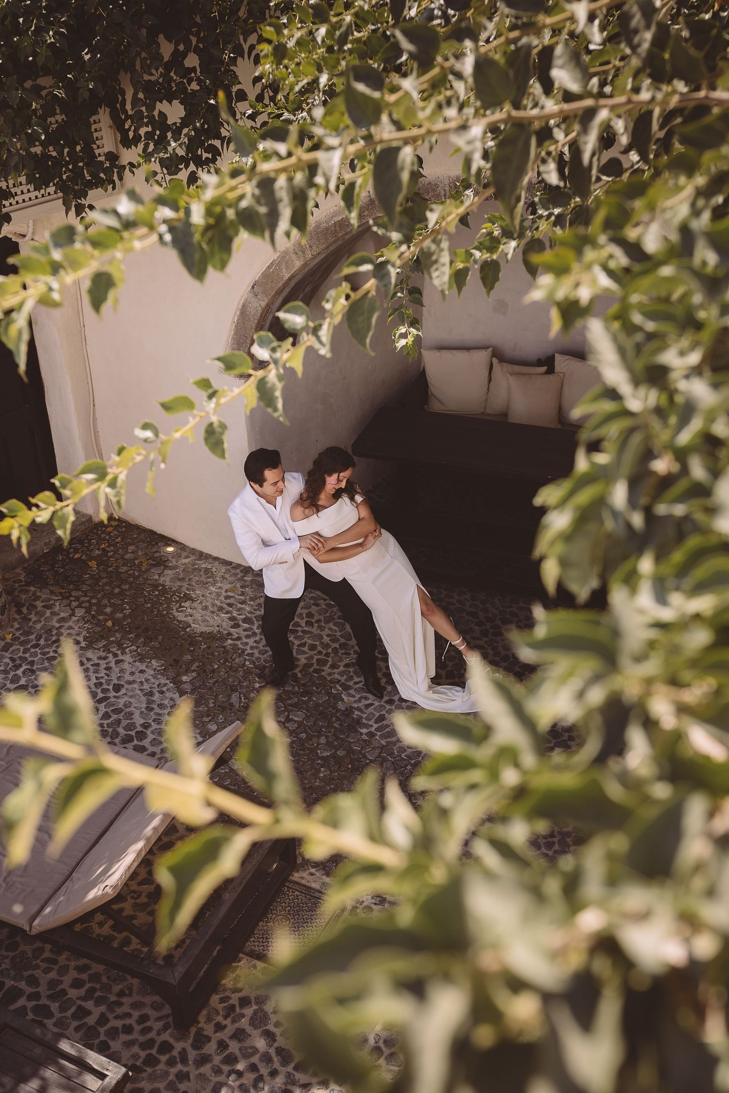 A Santorini destination wedding couple practice dancing in a courtyard viewed from above.