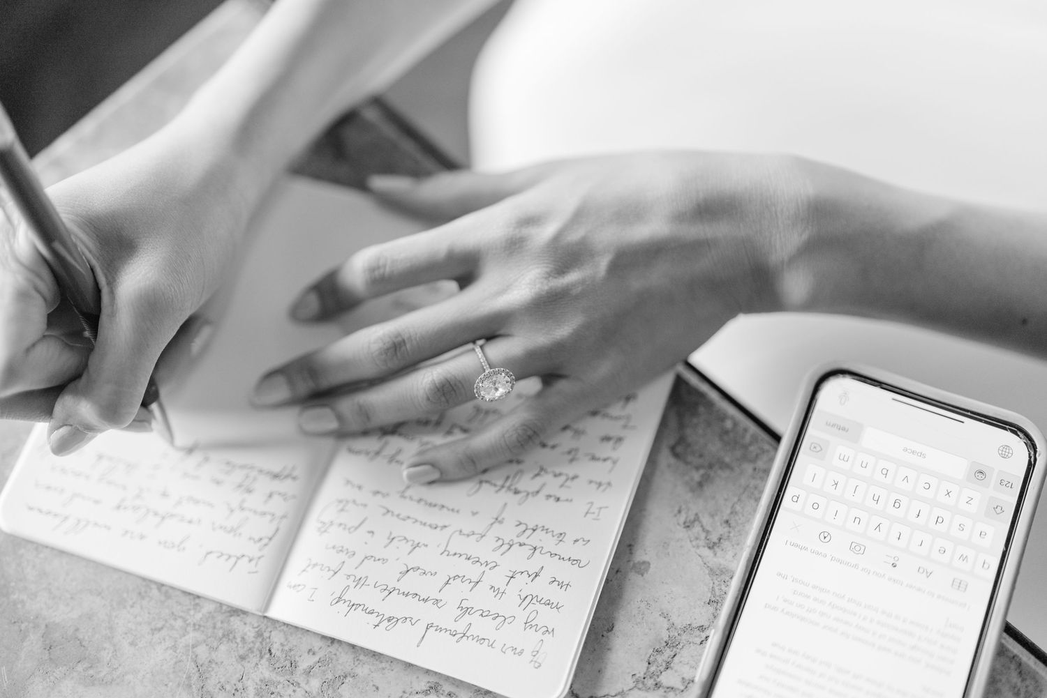 Close-up of hands writing in journal next to smartphone on white surface.
