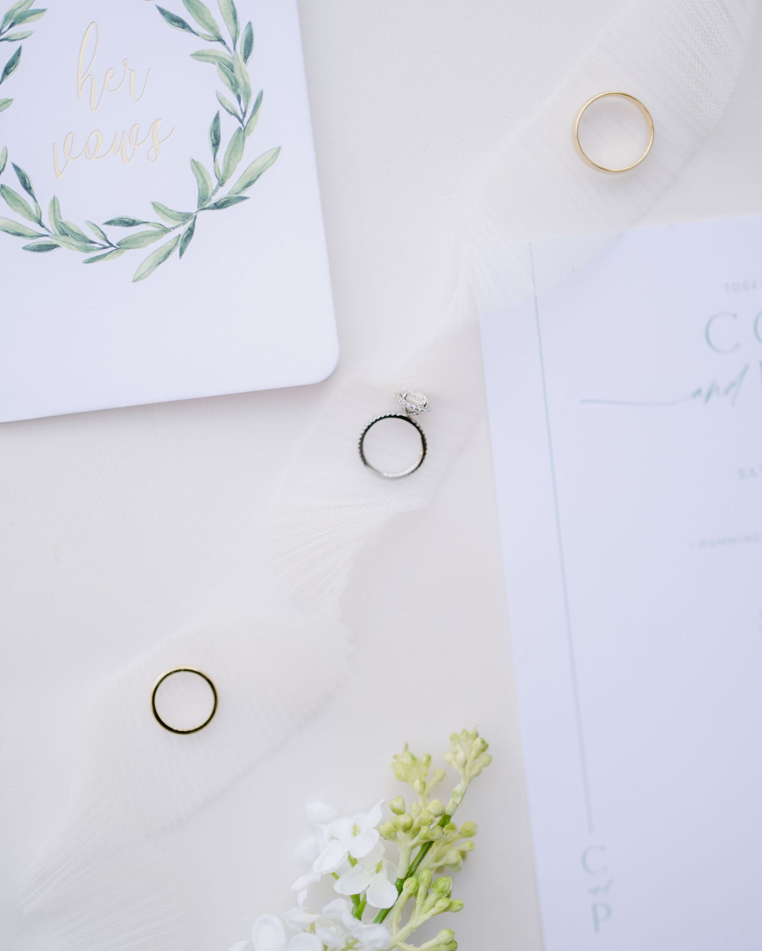 Wedding stationery with watercolor olive wreath and rings against white background with delicate flowers.